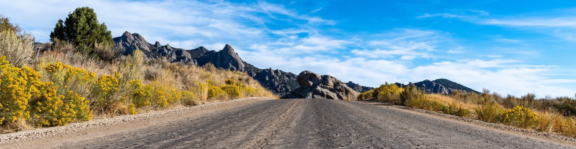 A car is driving down a dirt road with mountains in the background.