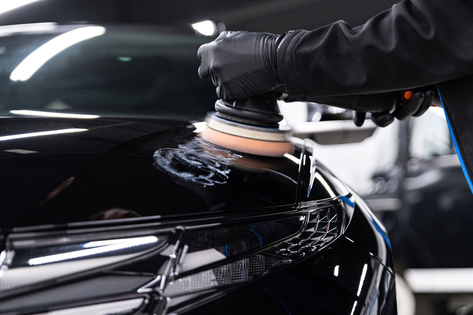 A person is polishing a black car with a machine.
