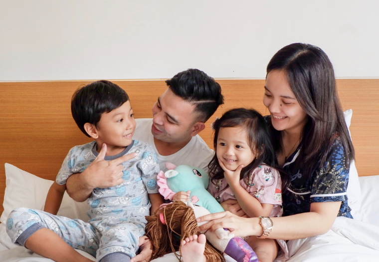 A family is sitting on a bed with a stuffed animal in a hotel in cabanatuan