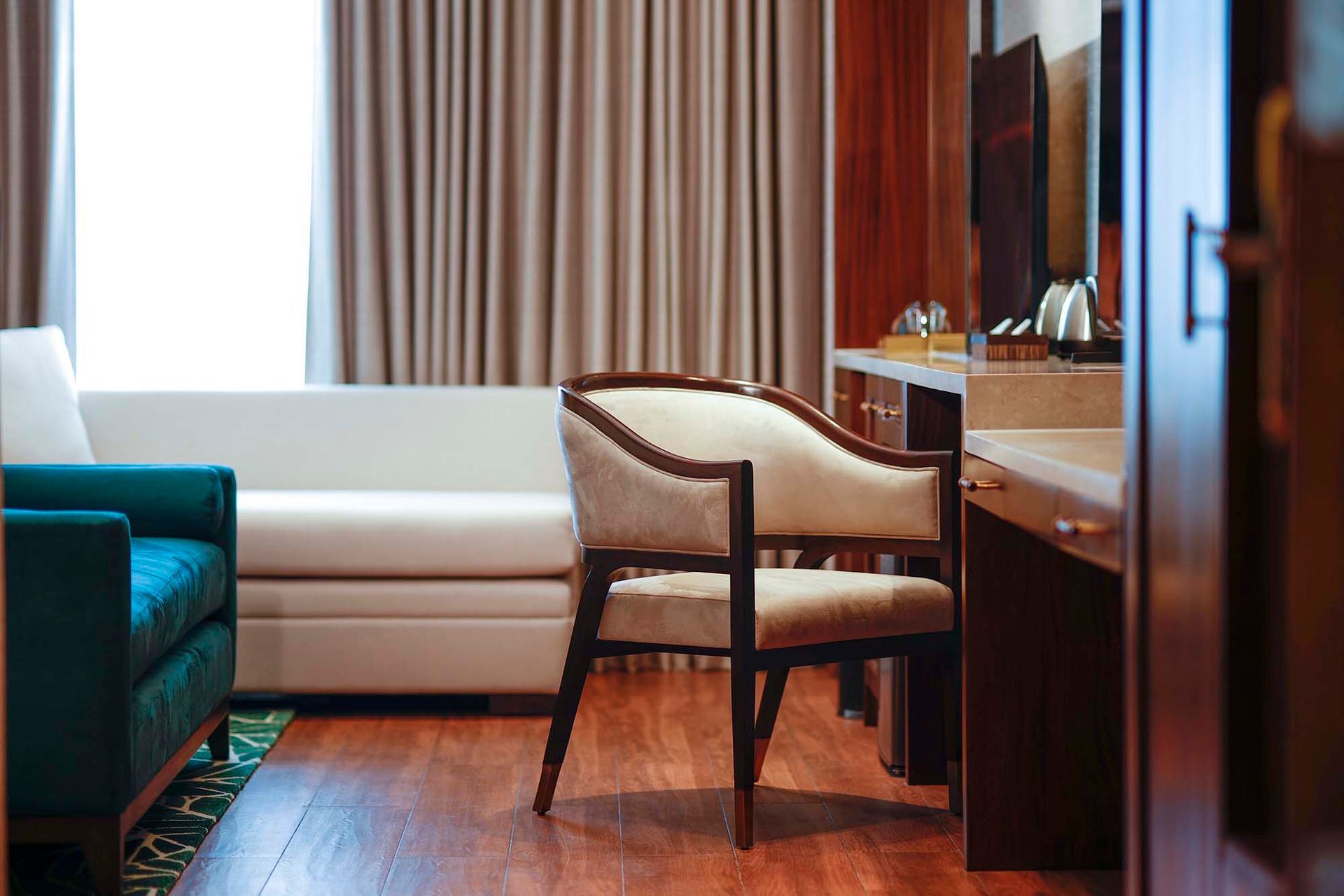 Hotel room interior with couch, chair, desk, window, and wood paneling.