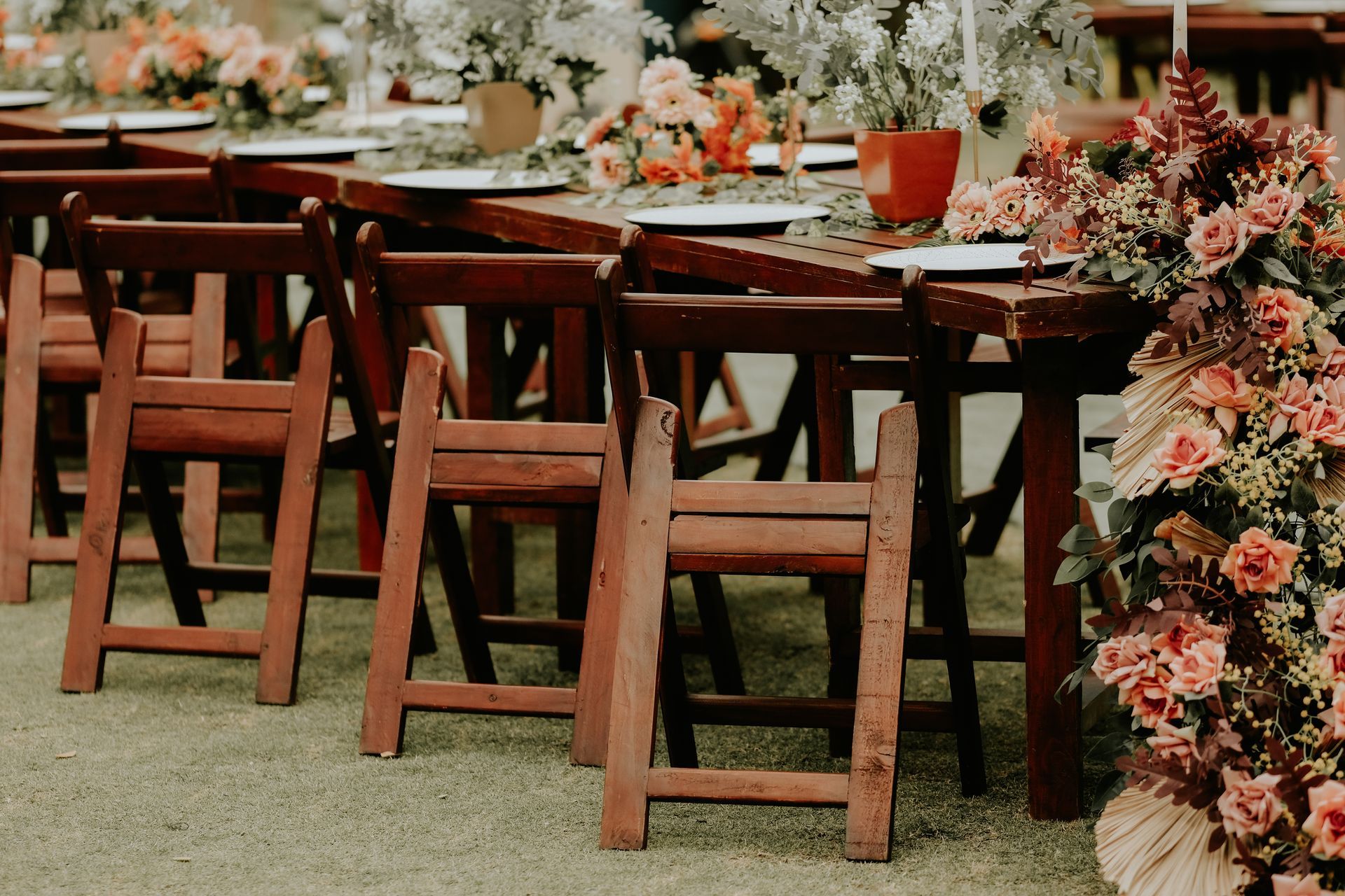 A row of wooden folding chairs sitting next to a table with flowers on it.