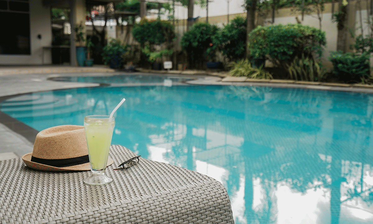 Straw hat and lemonade on a woven table beside a turquoise swimming pool
