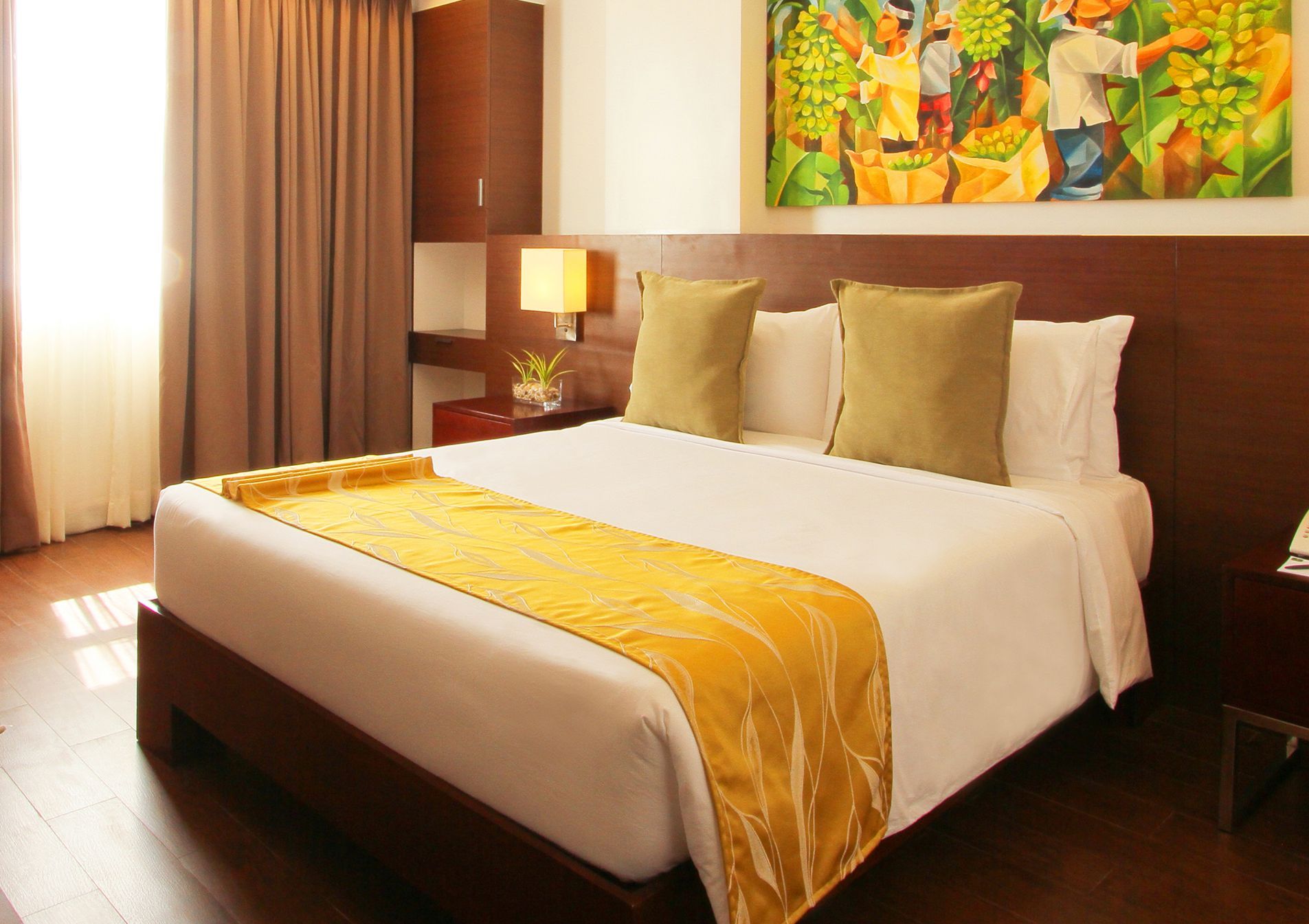 Hotel room with a large bed, brown headboard, yellow accents, and artwork.