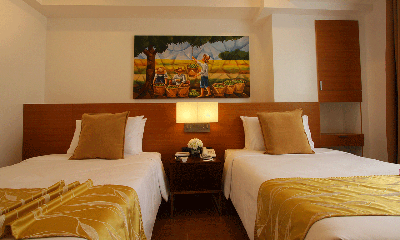 Two twin beds with gold and white linens, a nightstand, and a painting in a hotel room.