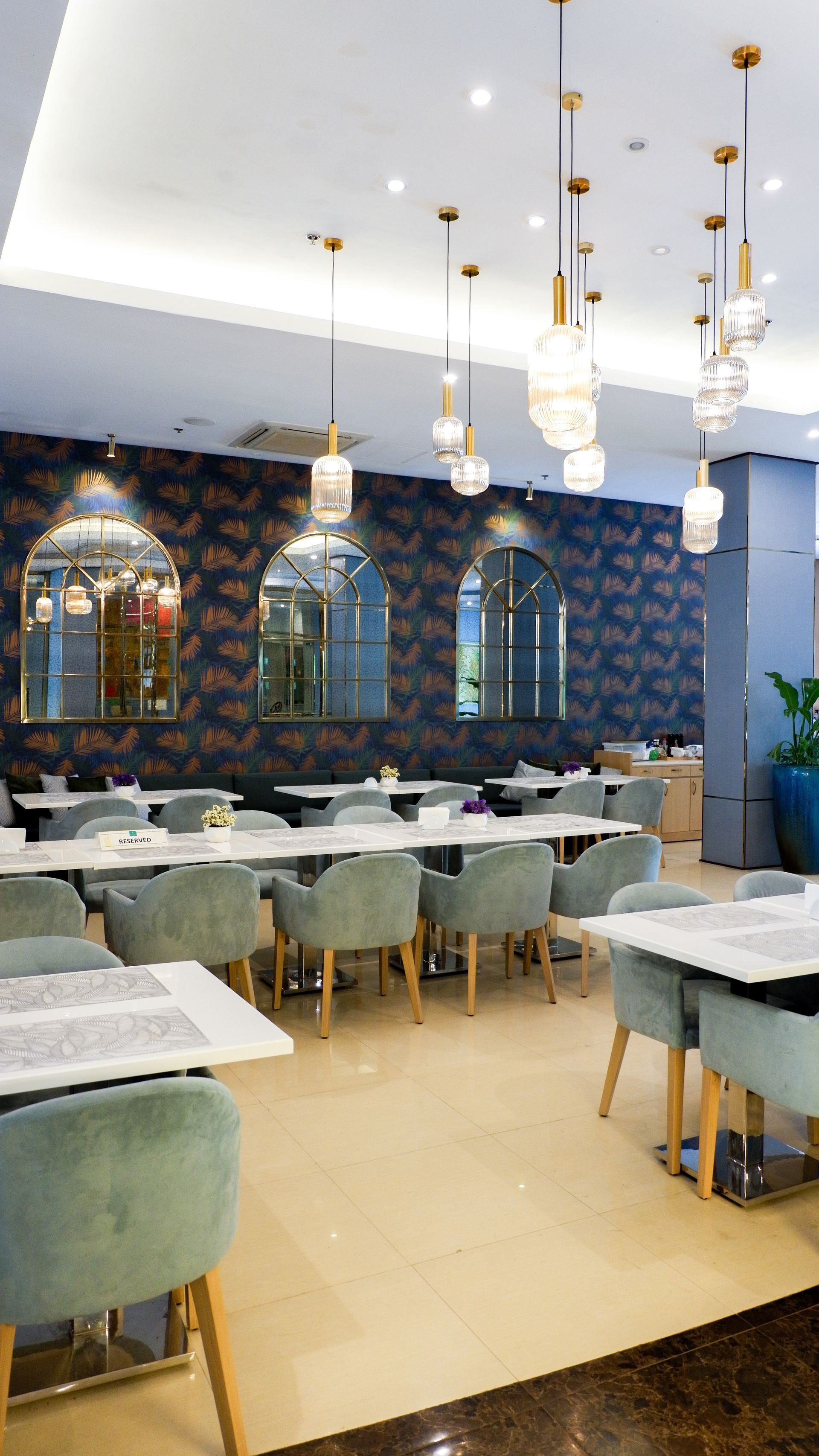 Elegant restaurant interior with tables, chairs, and decorative hanging lights. Blue and gold accents.