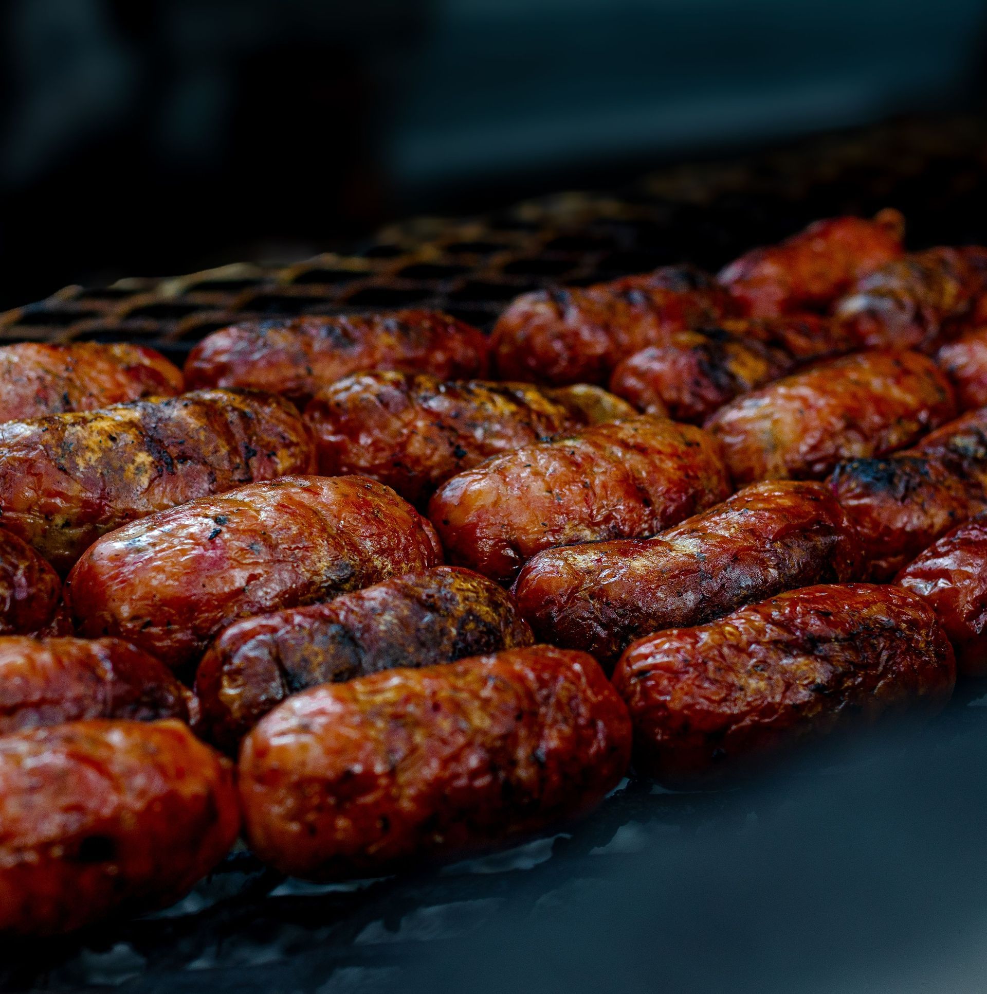 Rows of grilled sausages browning on a dark barbecue grill
