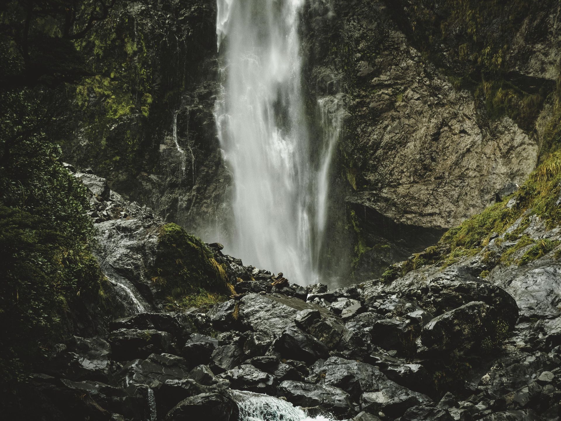 Waterfall cascading over rocks in a mossy, shaded landscape.