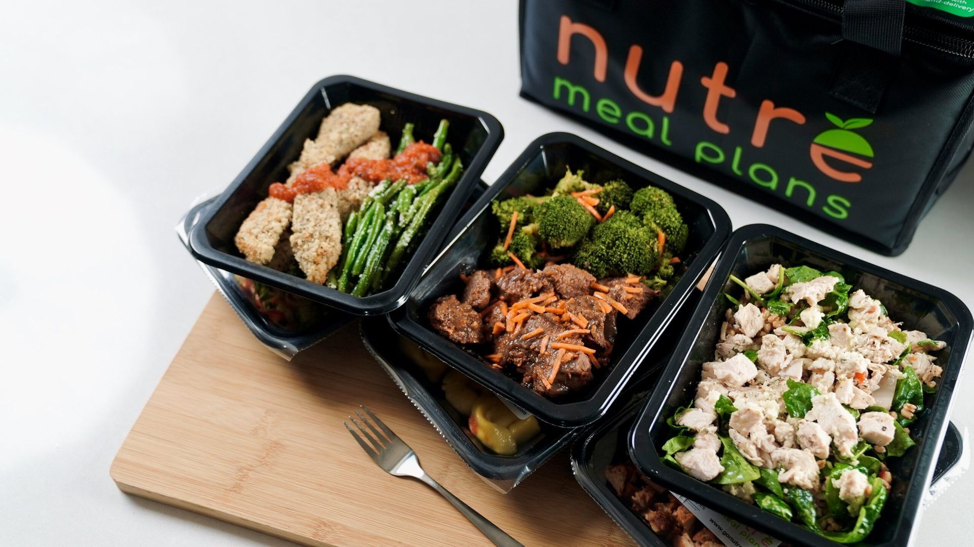 Prepared meal containers from Nutre Meal Plans next to a bag and a fork.