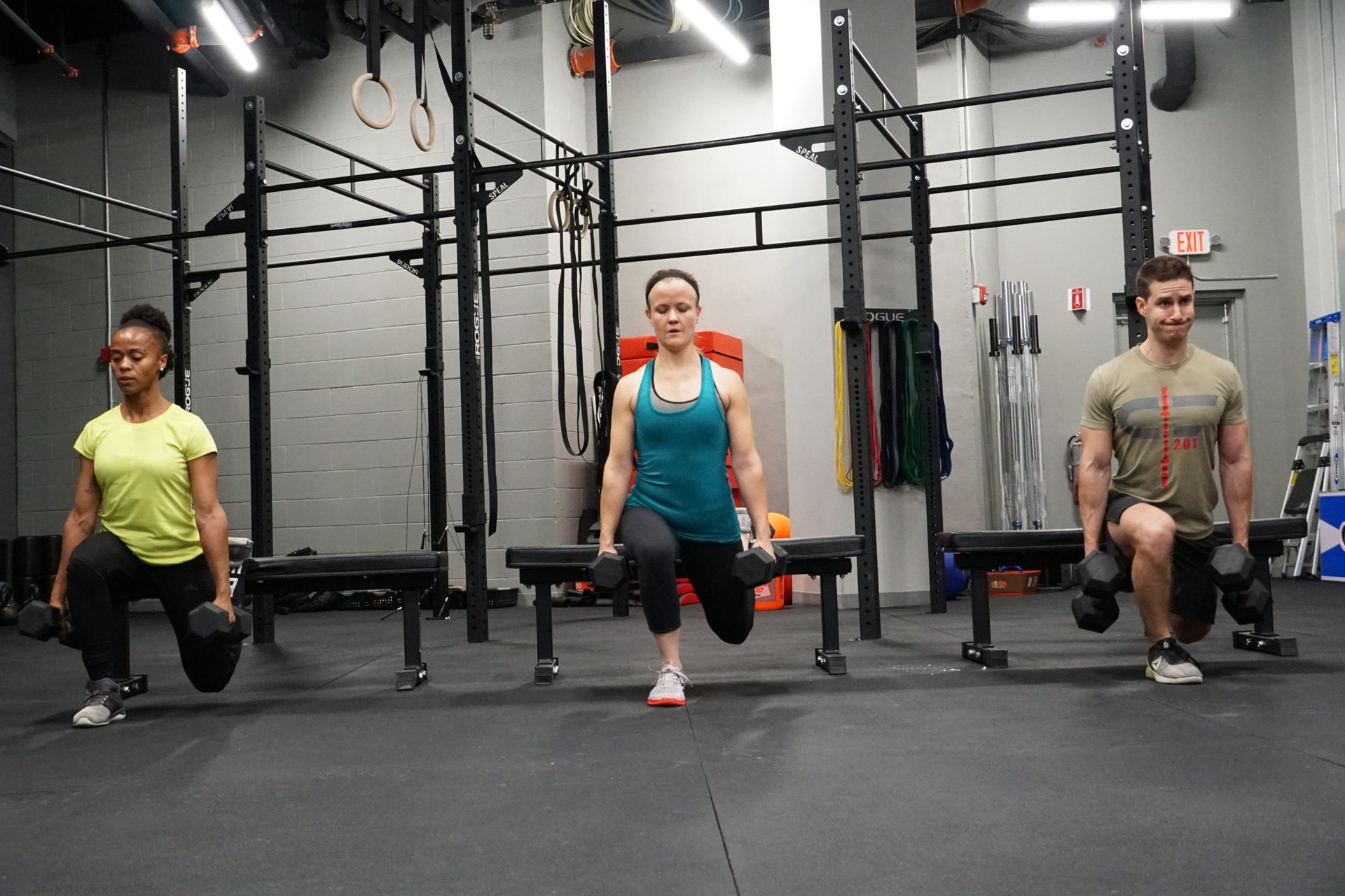 Three people doing dumbbell split squats in a gym.