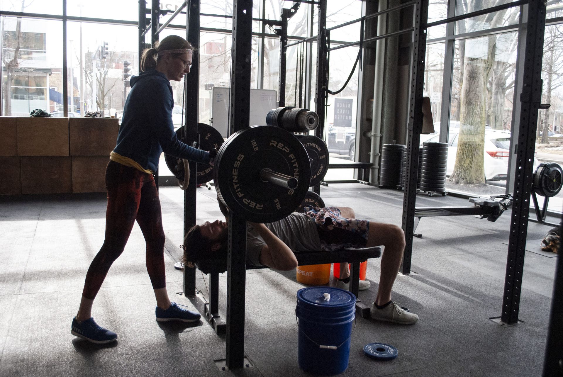 A woman spotting a man bench-pressing with a barbell in a gym.