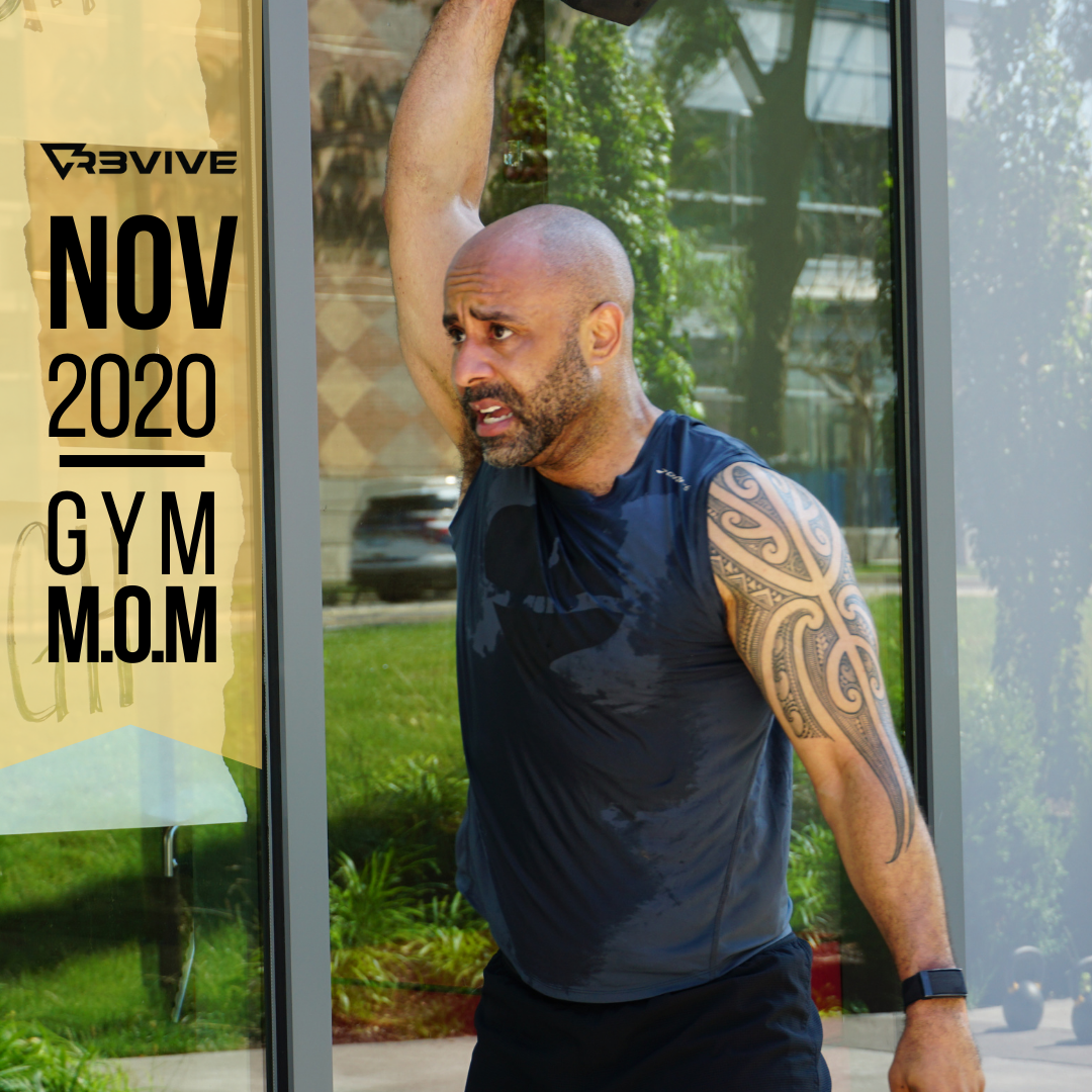 Man in gym clothes lifting dumbbell outside. Tattoo on arm, sweat visible. November 2020