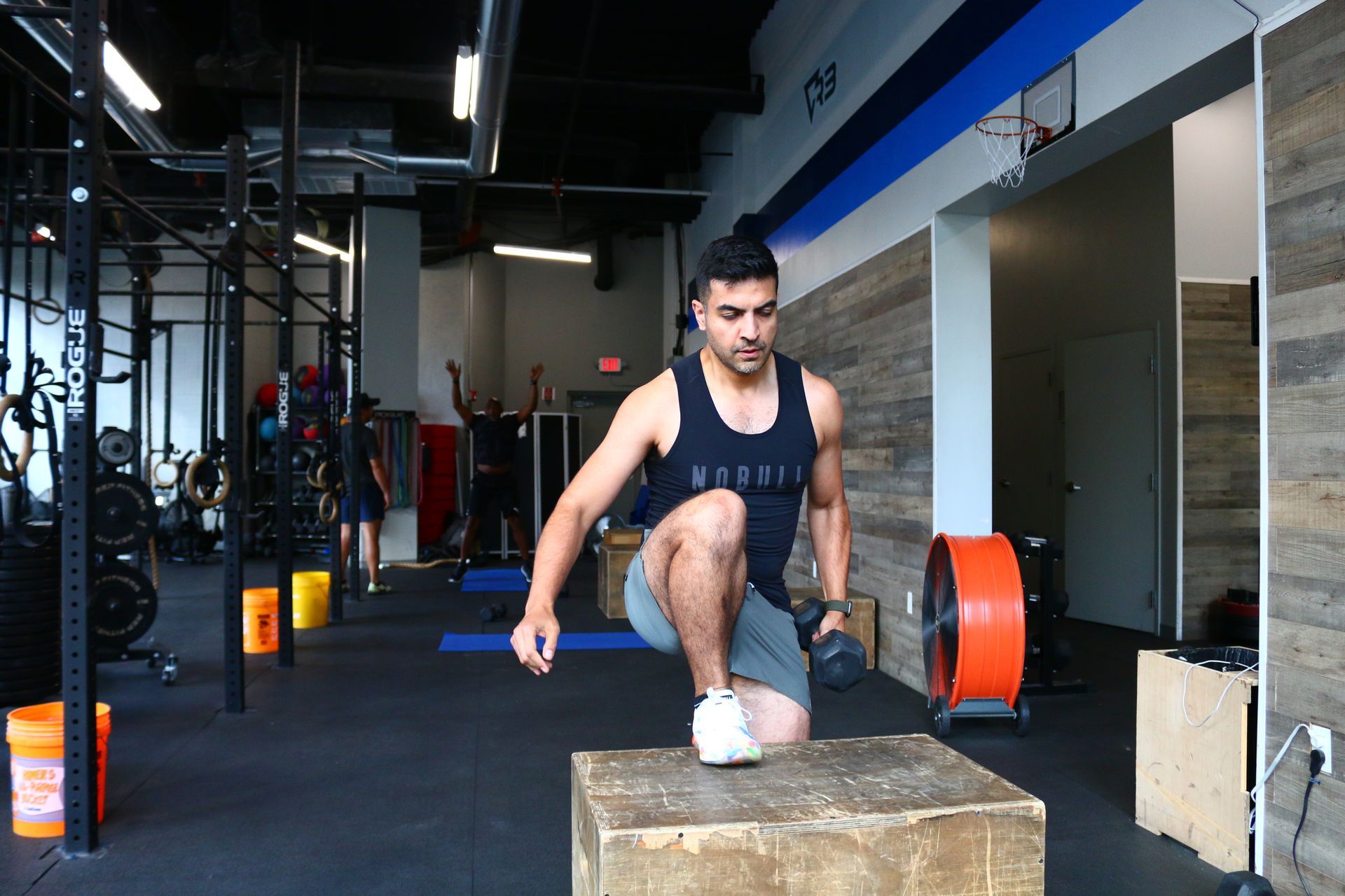 Man does dumbbell step-ups in a gym, using a wooden box.
