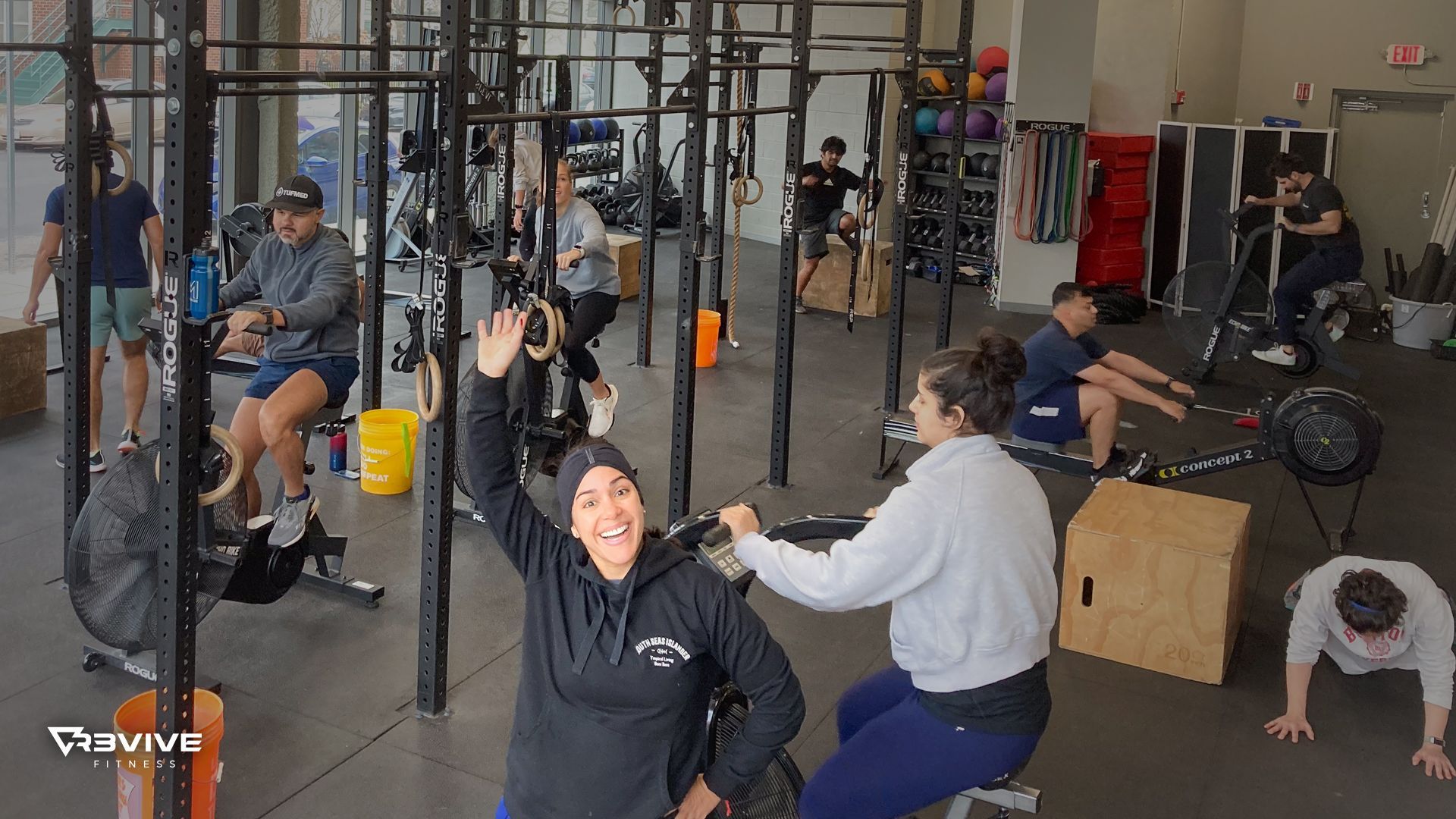 People working out in a gym, one woman in wheelchair smiles and waves.