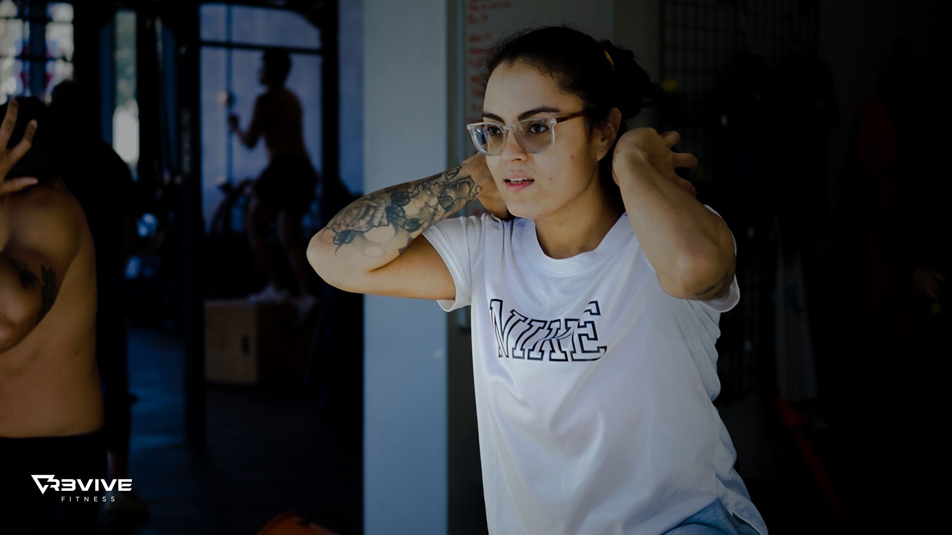 Woman in glasses and a white shirt stretching her neck in a gym.