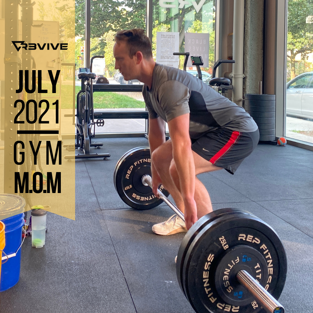 Man deadlifting in a gym, gray shirt, black shorts, barbell with weight plates, gym interior.