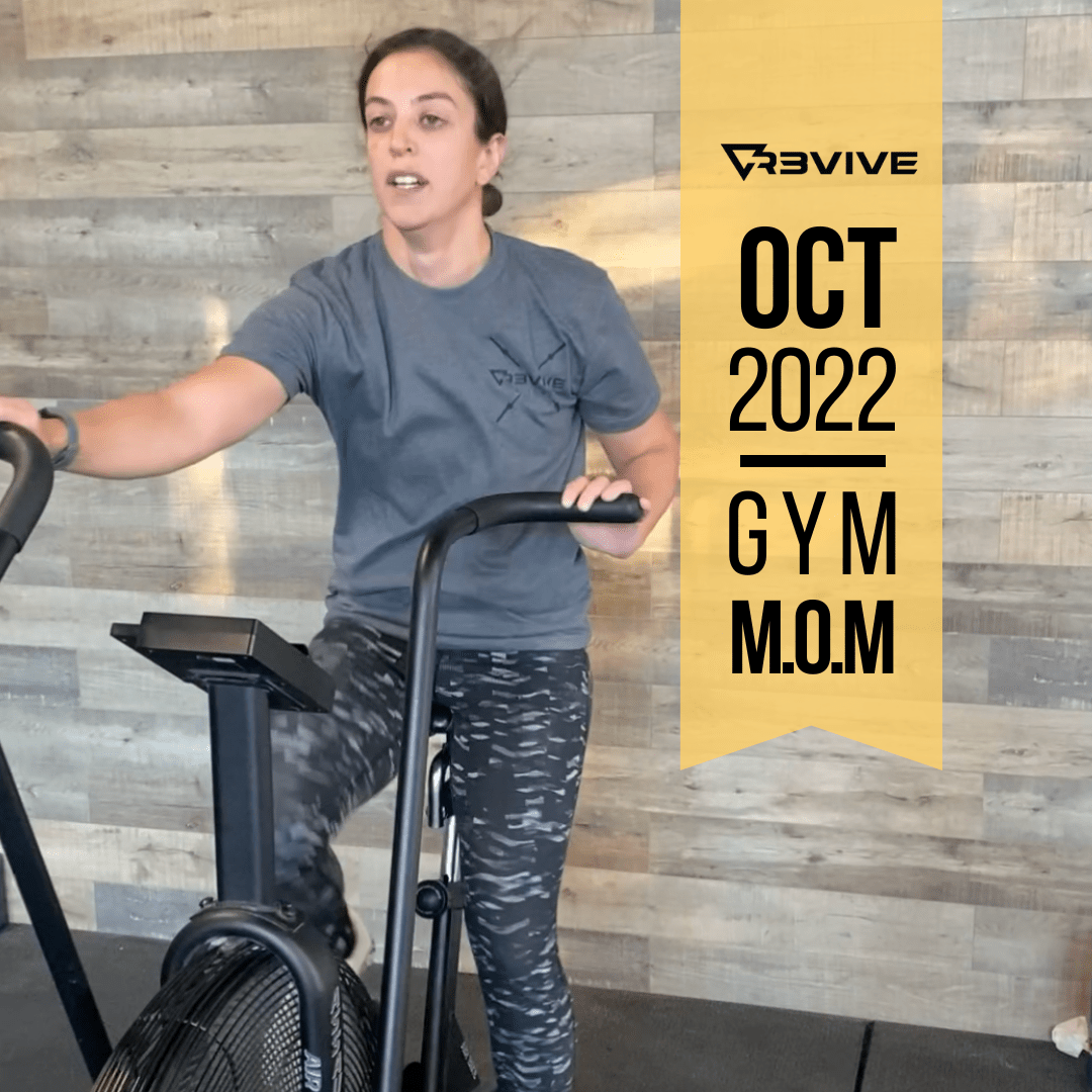 Woman on stationary bike at a gym. Text reads “Oct 2022 Gym M.O.M.” She wears a grey t-shirt and camo leggings.
