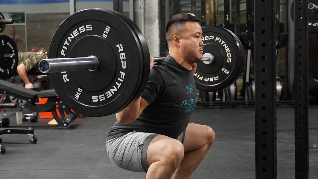 man squatting with barbell and plates