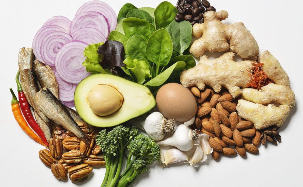 Assorted fresh, healthy foods: onion, spinach, avocado, egg, nuts, ginger, beans, sardines, broccoli.