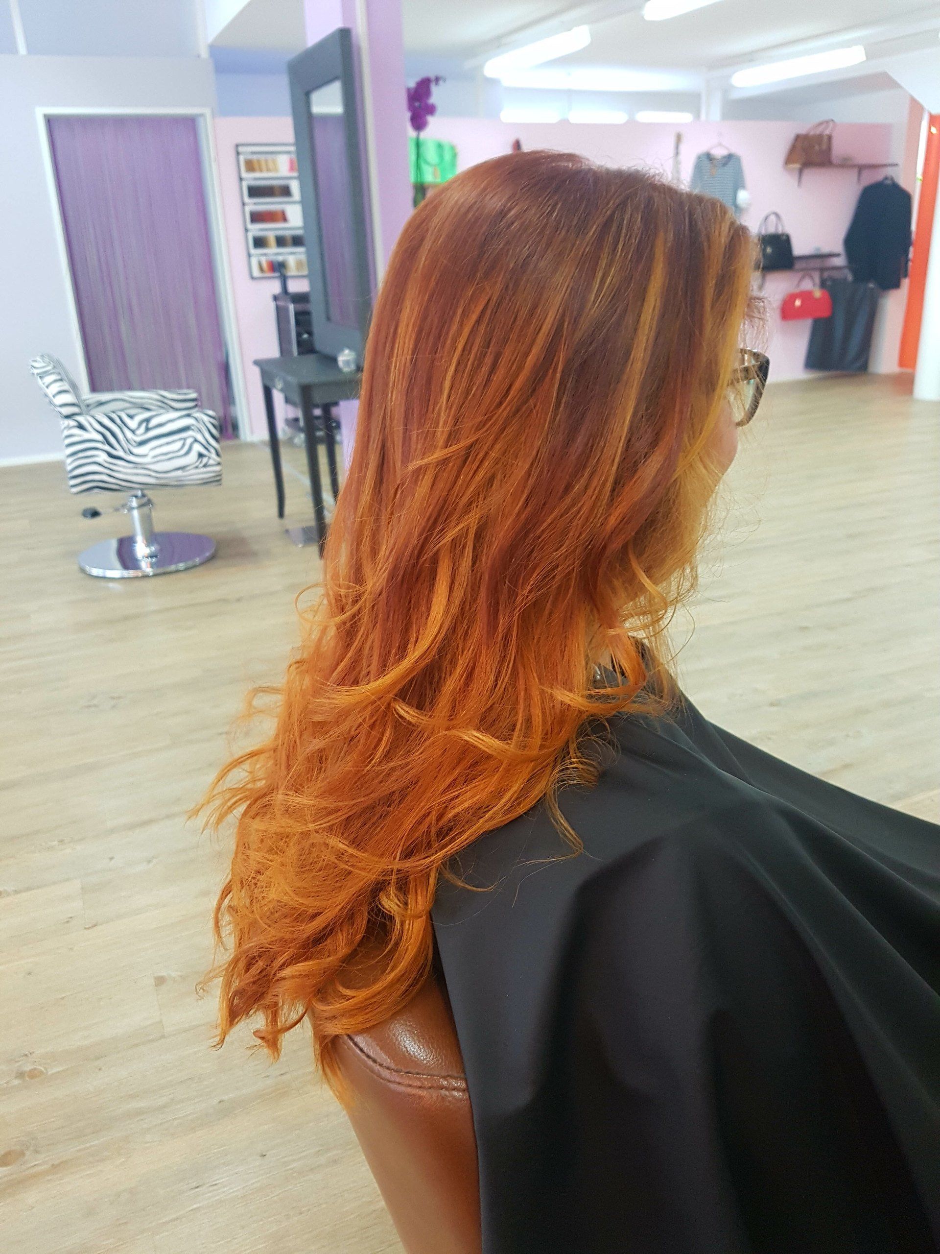 Eine Frau mit langen roten Haaren sitzt in einem Salon auf einem Stuhl.