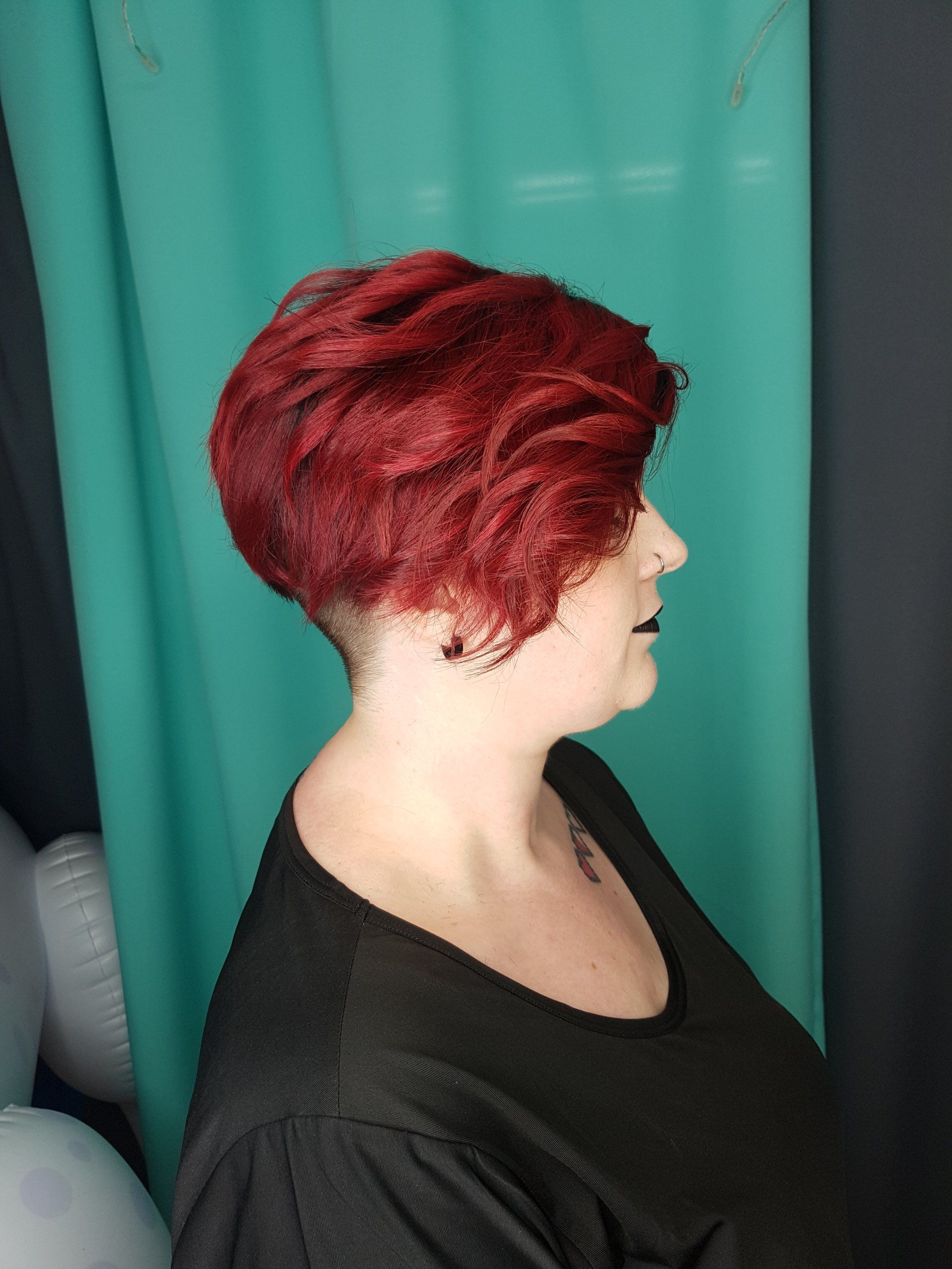 Eine Frau mit roten Haaren und einem schwarzen Hemd steht vor einem grünen Vorhang.