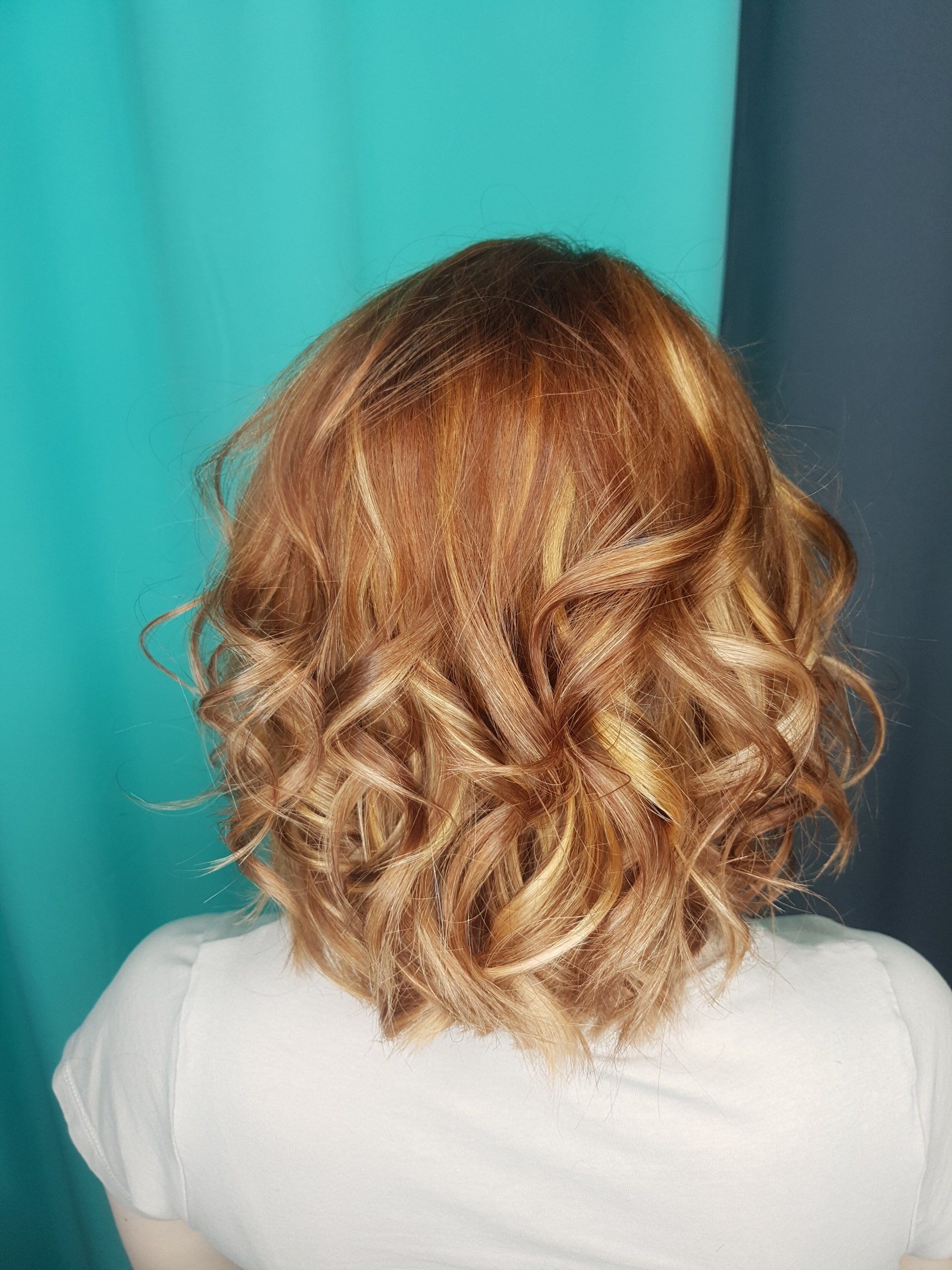 Der Hinterkopf einer Frau mit lockigem Haar und weißem Hemd.