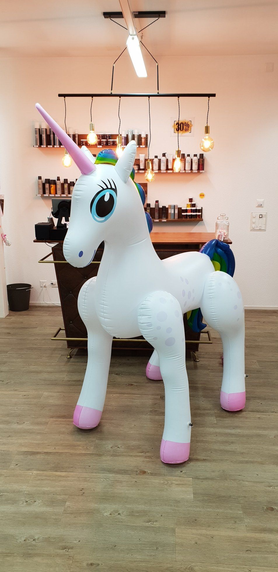 Ein großes aufblasbares Einhorn steht auf einem Holzboden in einem Raum.