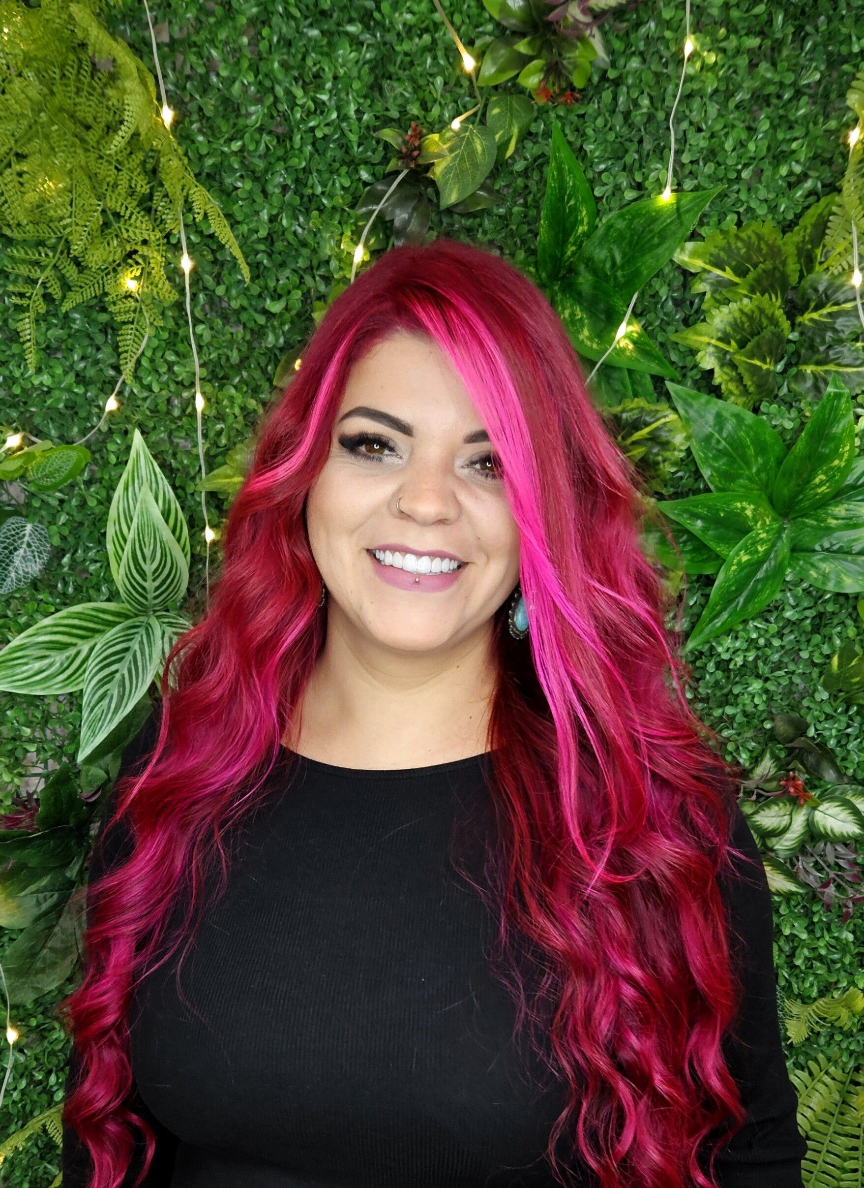 Eine Frau mit langen roten Haaren lächelt vor einer grünen Wand.