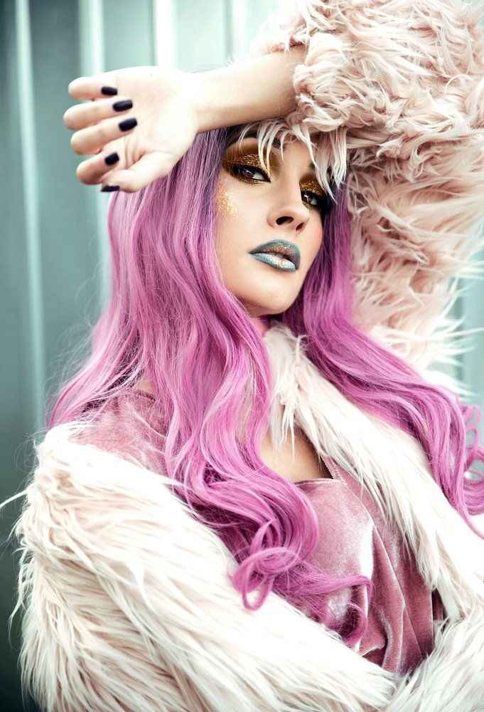 Eine Frau mit lila Haaren und schwarzen Nägeln trägt einen Pelzmantel.