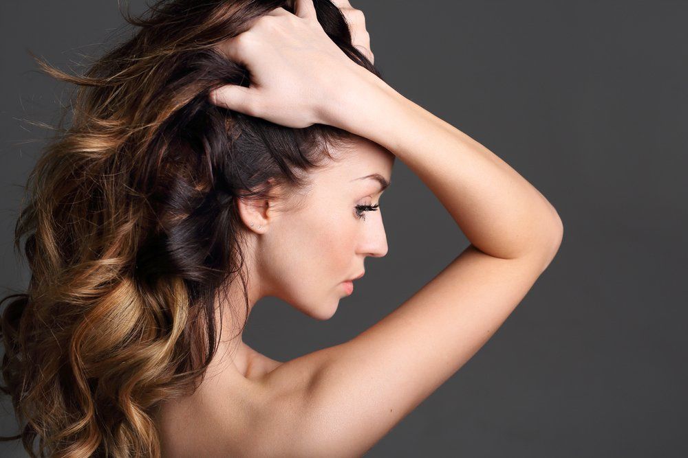 Eine Frau mit langen Haaren berührt ihr Haar mit der Hand.