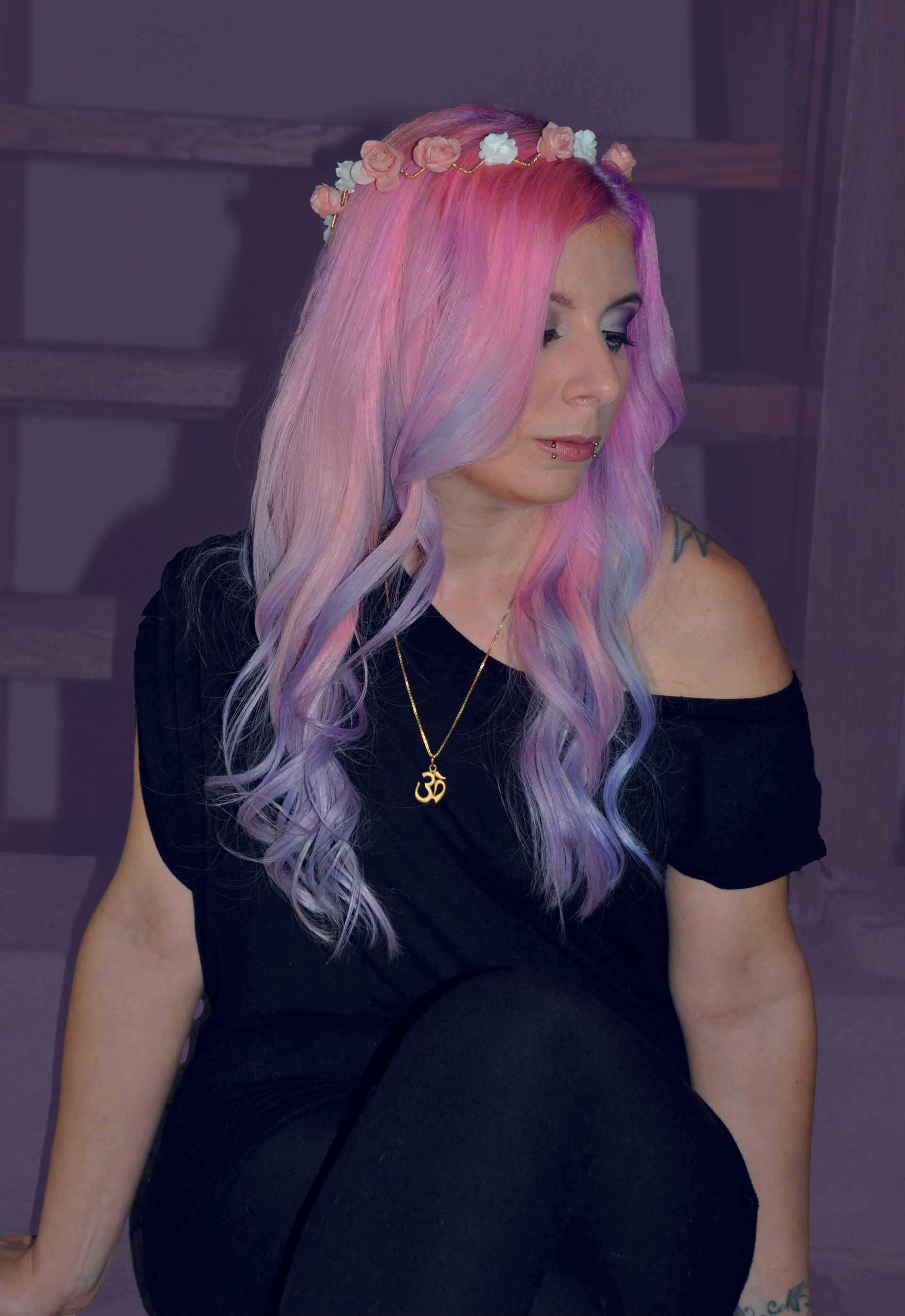 Eine Frau mit rosa und violettem Haar trägt ein schwarzes Kleid und eine Halskette.