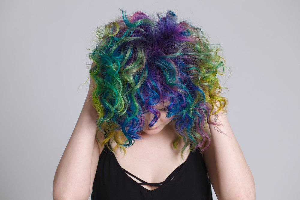 Eine Frau mit buntem, lockigem Haar bedeckt ihr Gesicht mit den Händen.