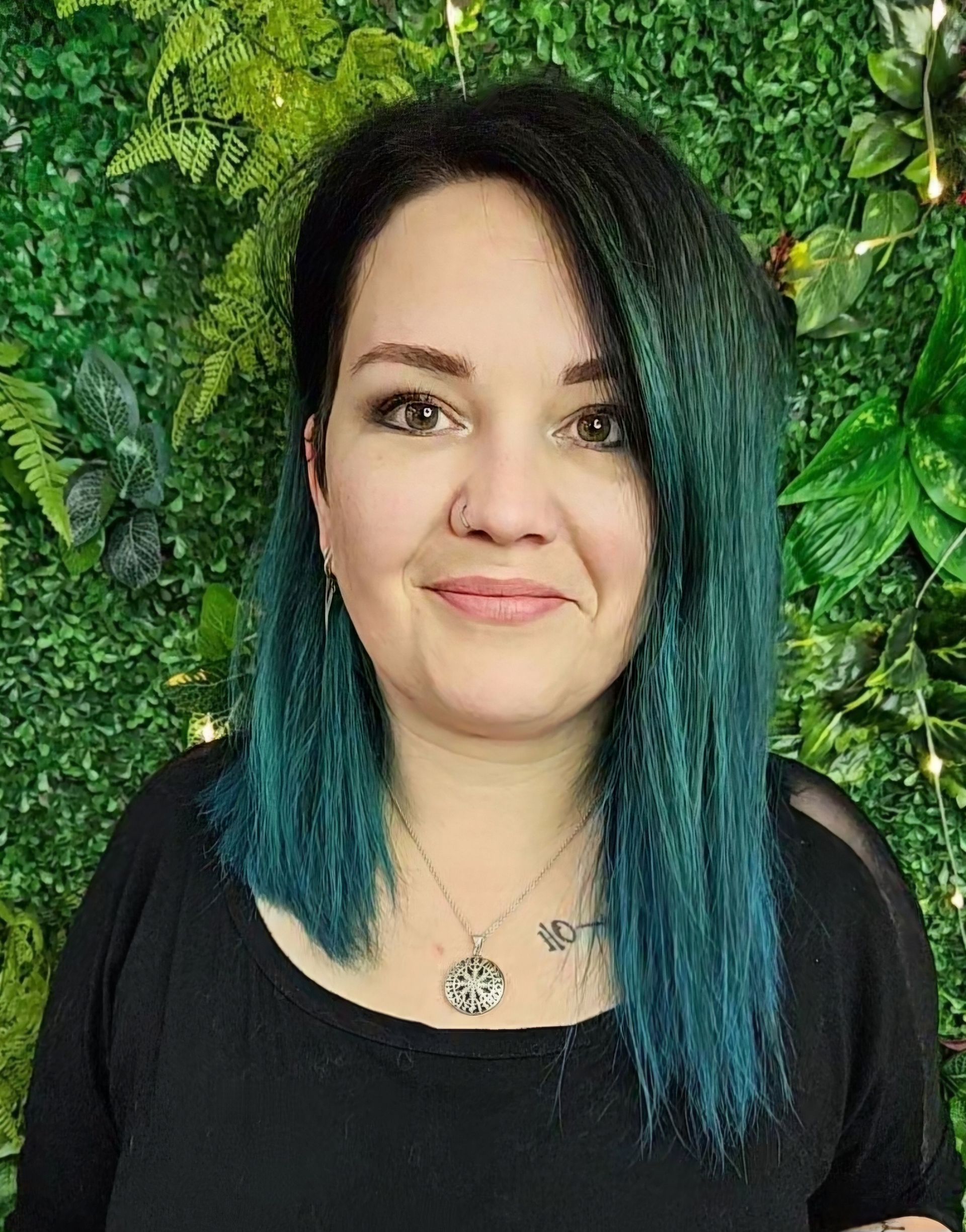 Eine Frau mit blauen Haaren trägt ein schwarzes Hemd und eine Halskette.