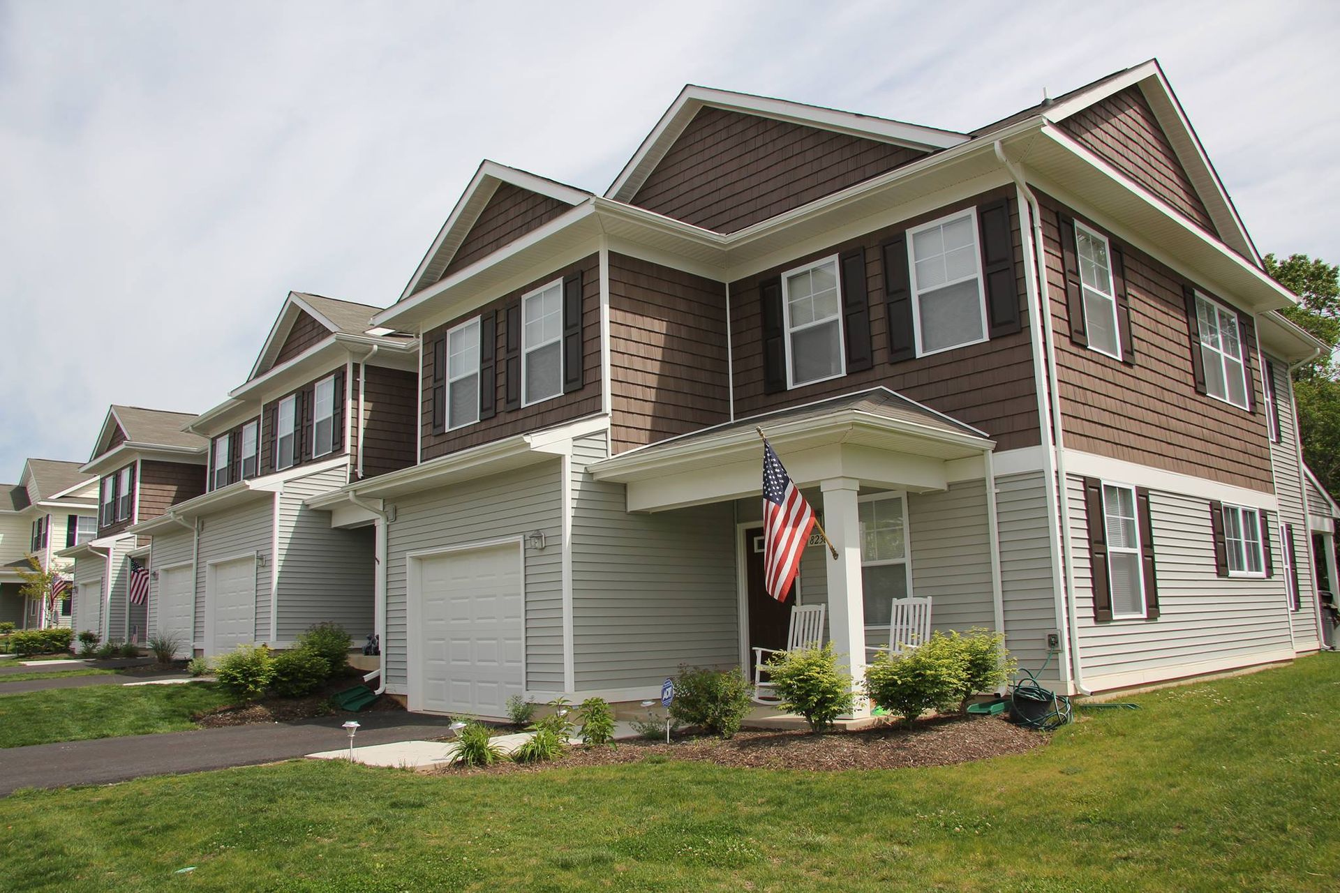 Townhomes with gray siding, brown brick-like panels, and white trim. American flag hangs on front porch.