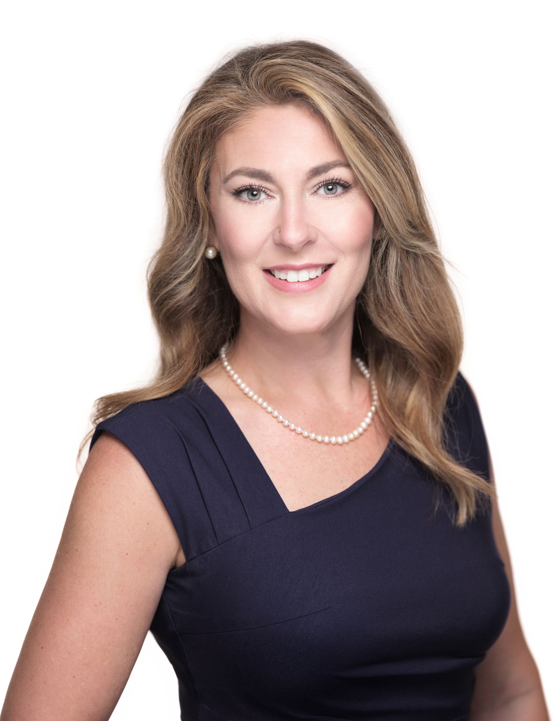 A woman wearing a blue dress and a pearl necklace is smiling for the camera.