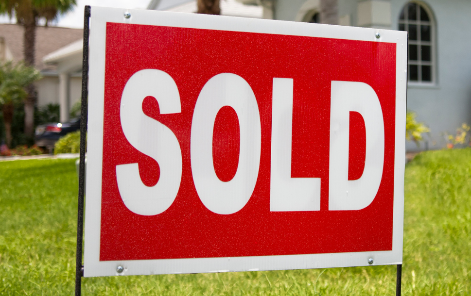 A red and white sold sign is in the grass in front of a house.