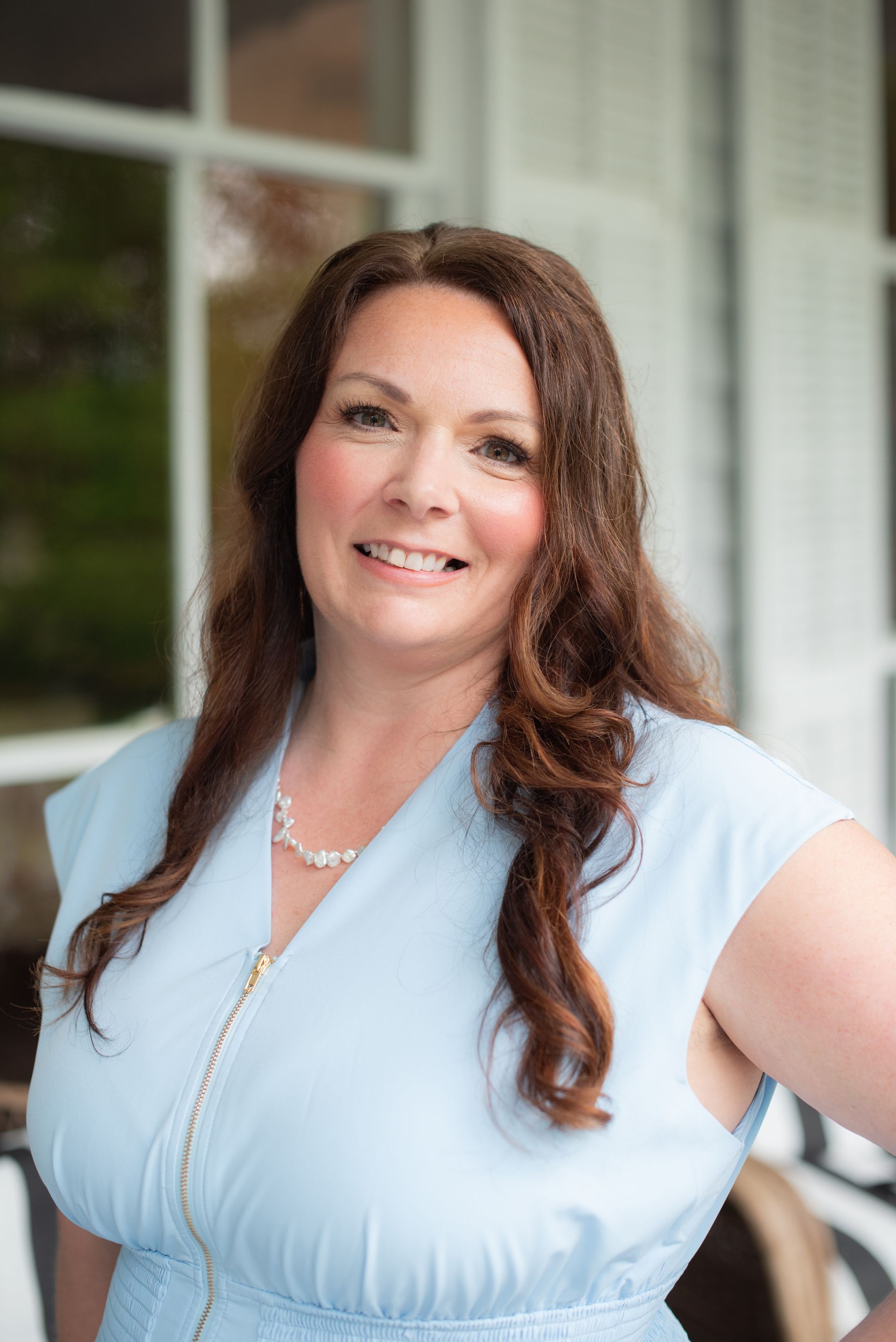 A woman in a light blue dress and necklace is smiling for the camera.