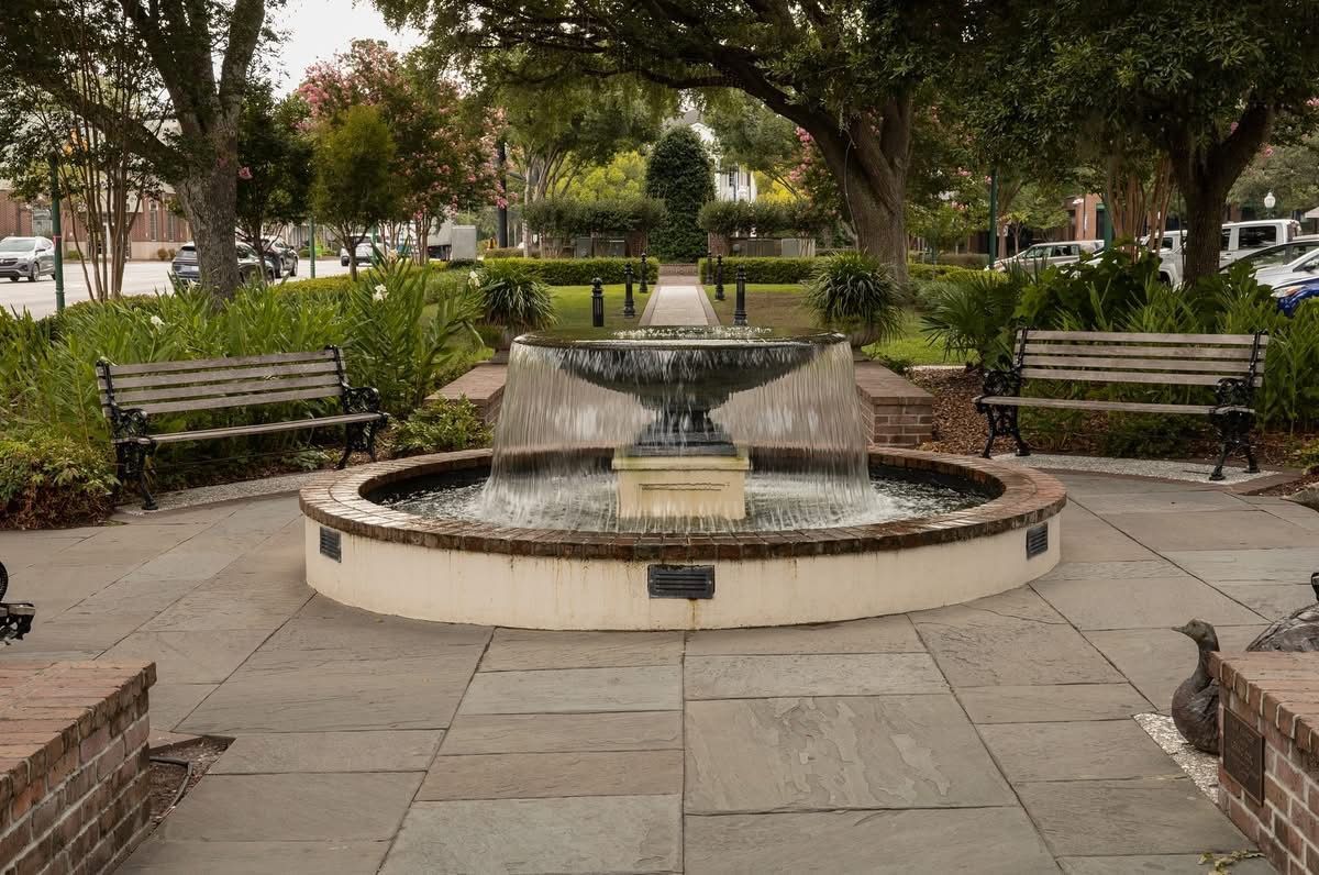 There is a fountain in the middle of a park surrounded by benches.