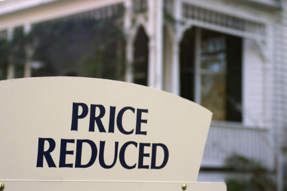 A sign that says price reduced in front of a house