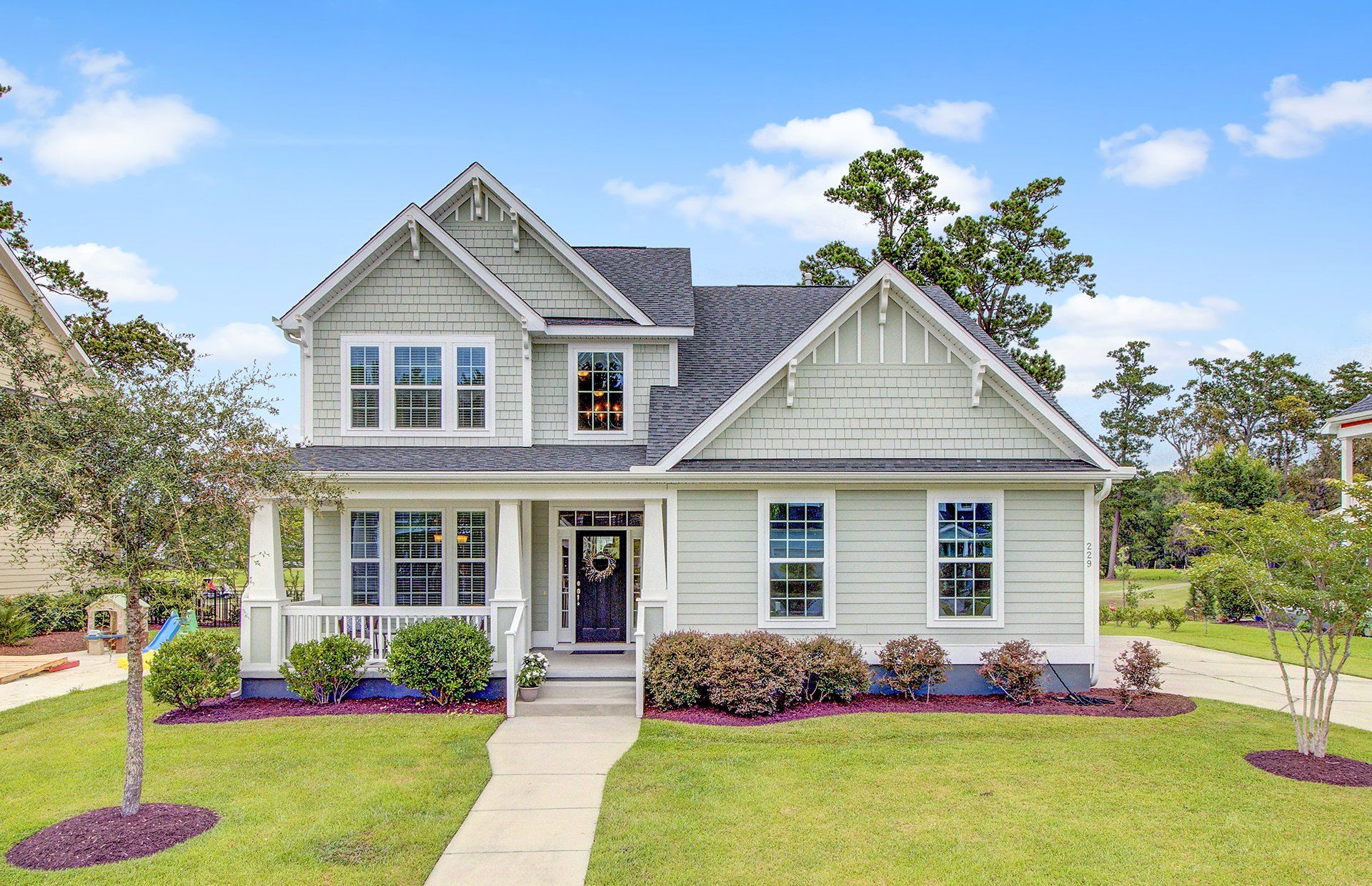 A white house with a black roof is sitting on top of a lush green field.