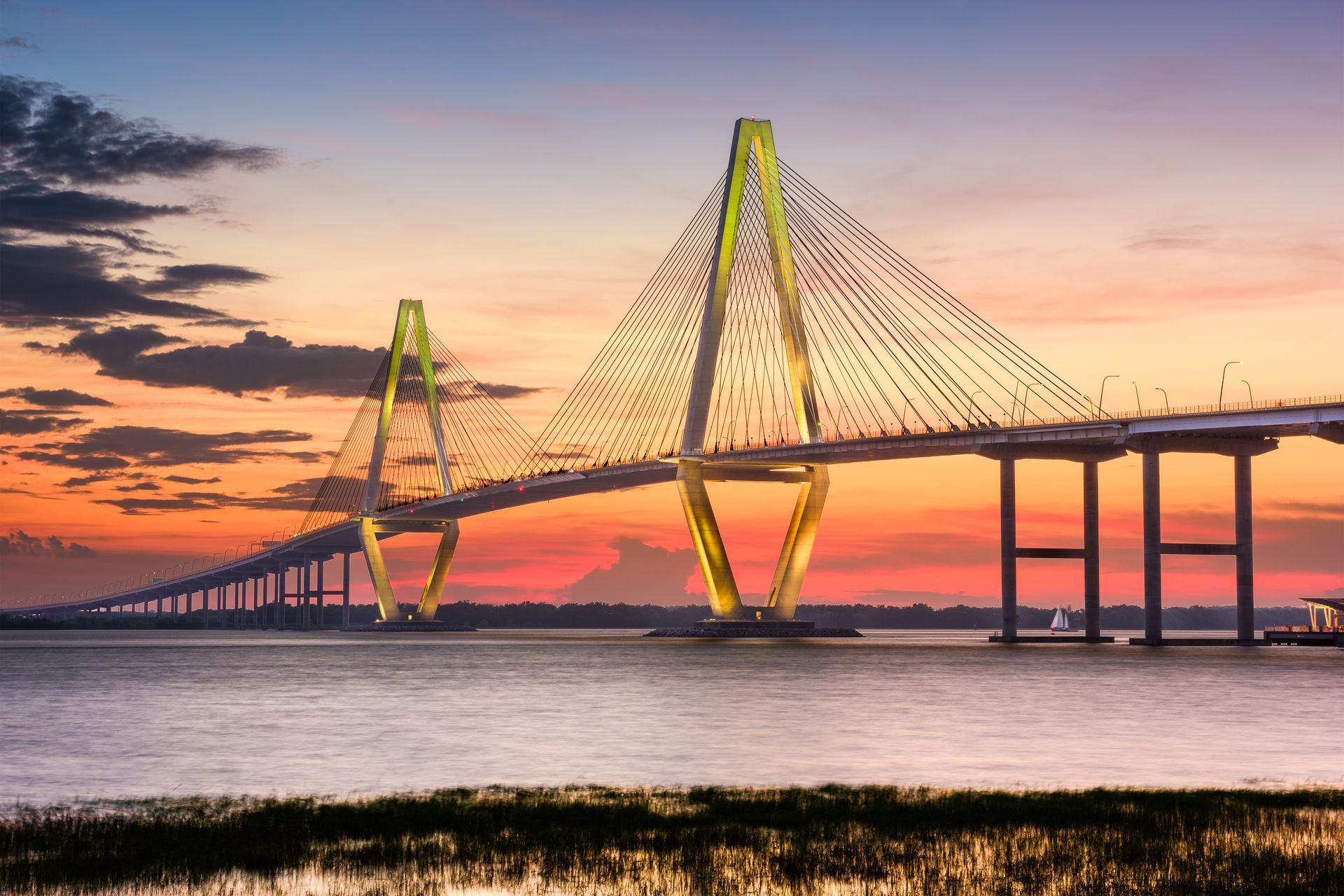 A cable-stayed bridge over water at sunset. The sky is orange and purple; the bridge is lit up.