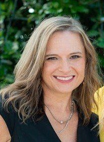 A woman is smiling for the camera while wearing a black shirt and a necklace.