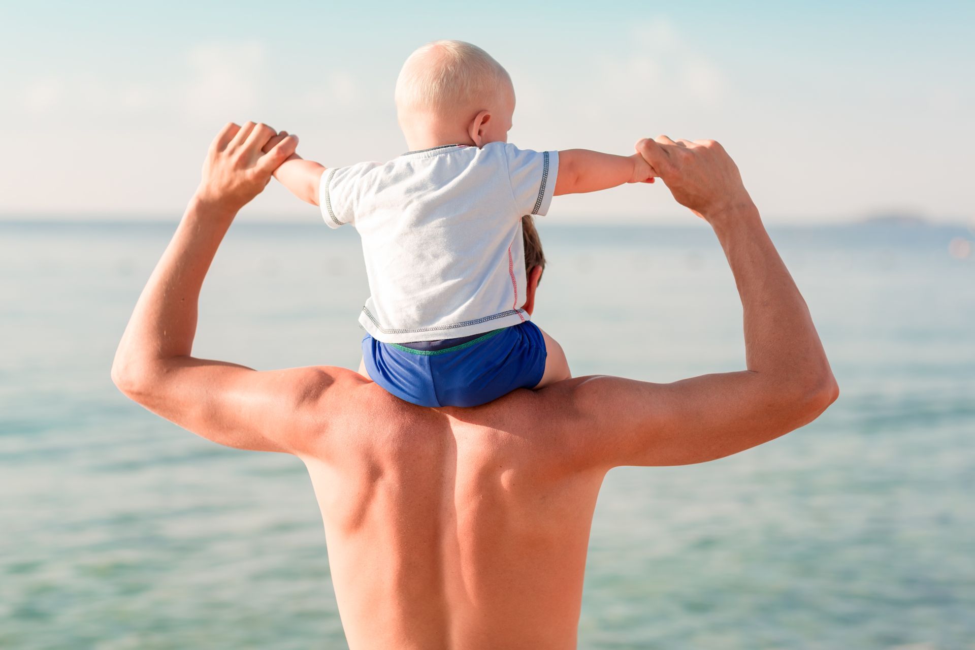 A dad carries a small child on their shoulders at the beach.