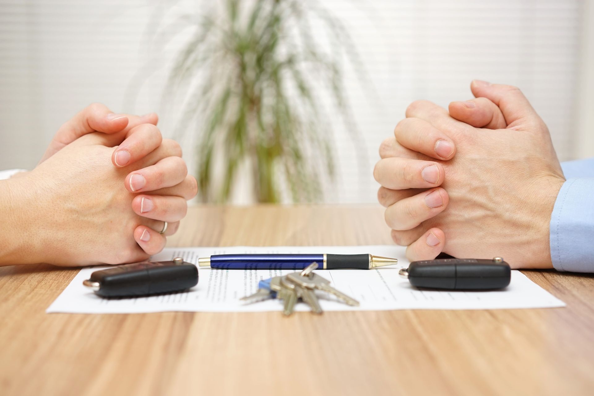 Two people’s hands clasped in a meeting across a table with car keys and documents between them