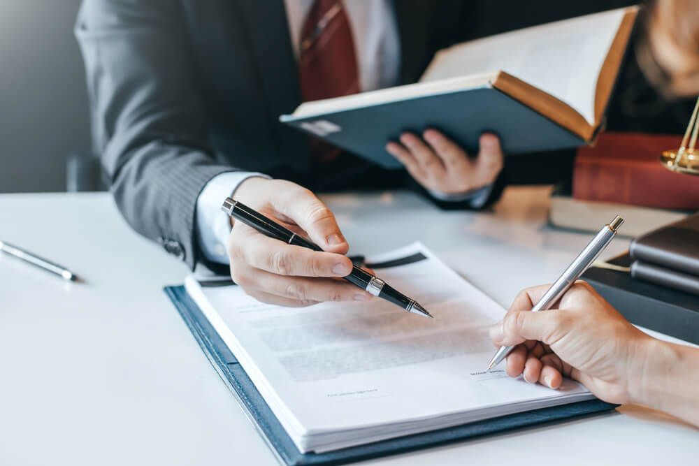 Lawyer pointing to a document as a person signs it with a pen, in an office.
