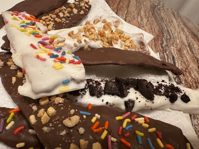 Chocolate-covered banana slices with various toppings: sprinkles, nuts, and cookie crumbs.