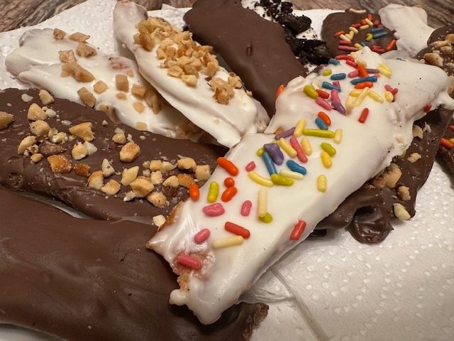 Various chocolate-covered treats, some with nuts, sprinkles, or cookies, on a white paper towel.