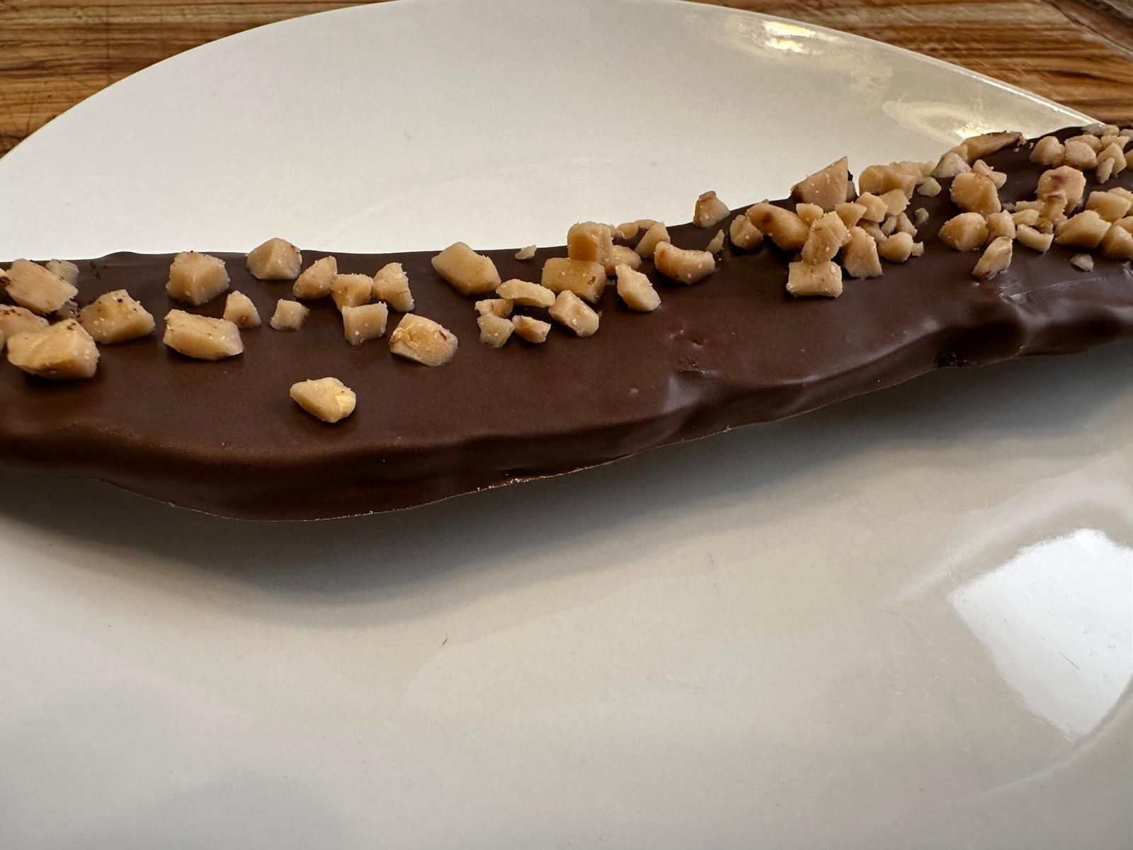 Chocolate-covered banana with toffee bits on a white plate.