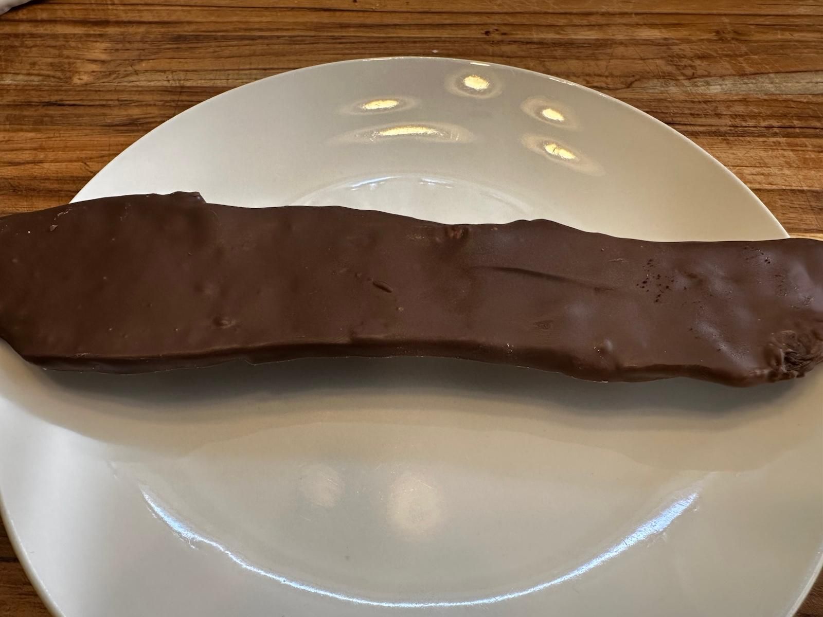 Chocolate-covered bar on a white plate, sitting on a wooden table.