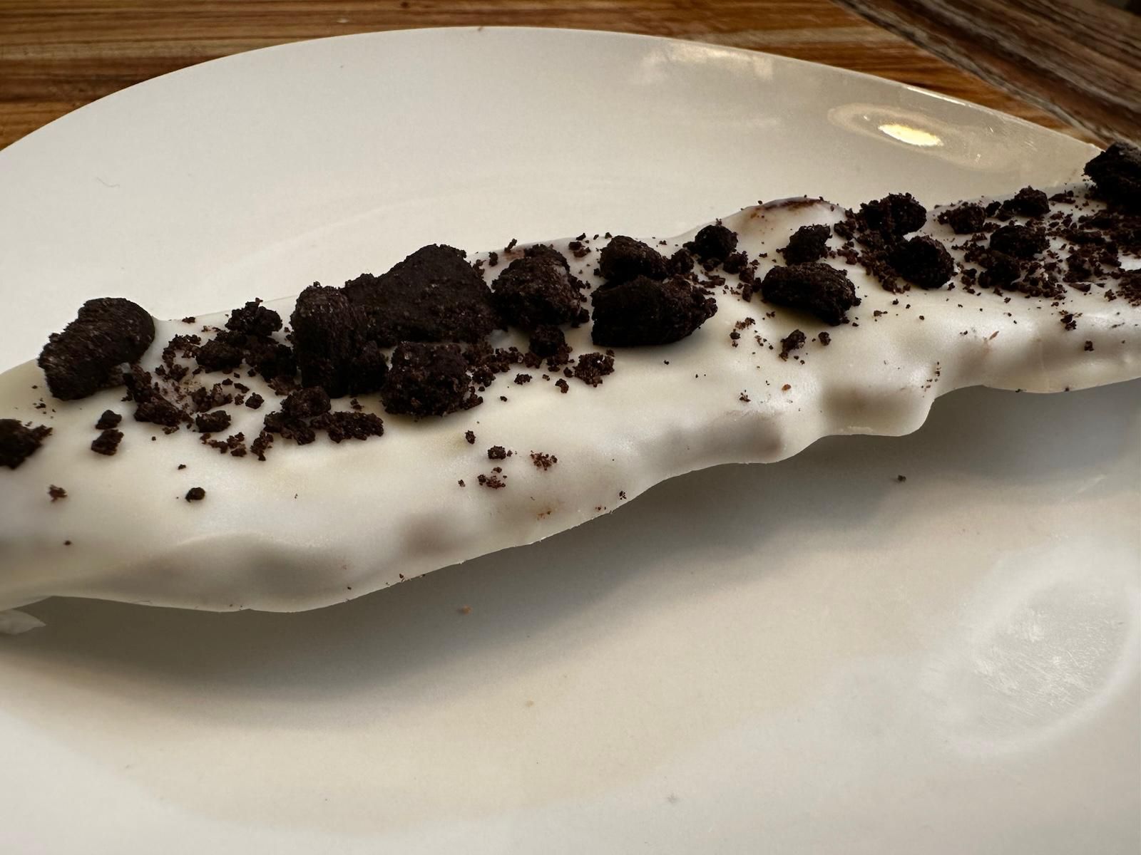 White chocolate-covered banana topped with crushed Oreo cookies on a white plate.