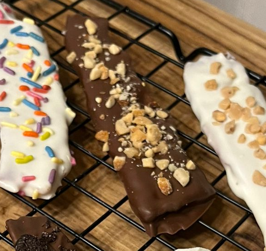 Chocolate-covered frozen bananas with sprinkles and chopped nuts, resting on a cooling rack.